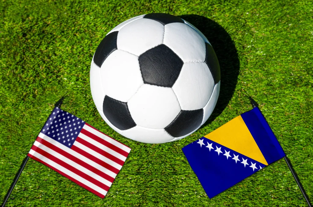 USA gegen Bosnien und Herzegowina mit Fußball und Nationalflaggen auf grünem Rasen als Motiv für ein internationales Fußball-Länderspiel.