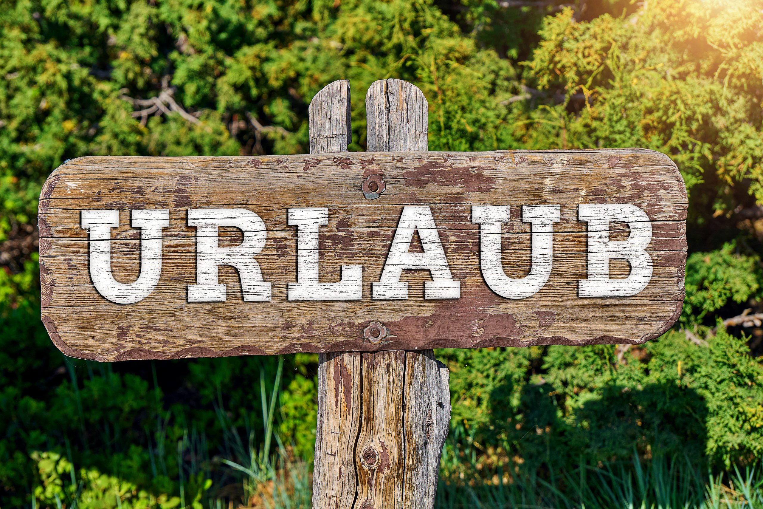 urlaub bilder: holzschild mit der aufschrift urlaub vor einer grünen landschaft