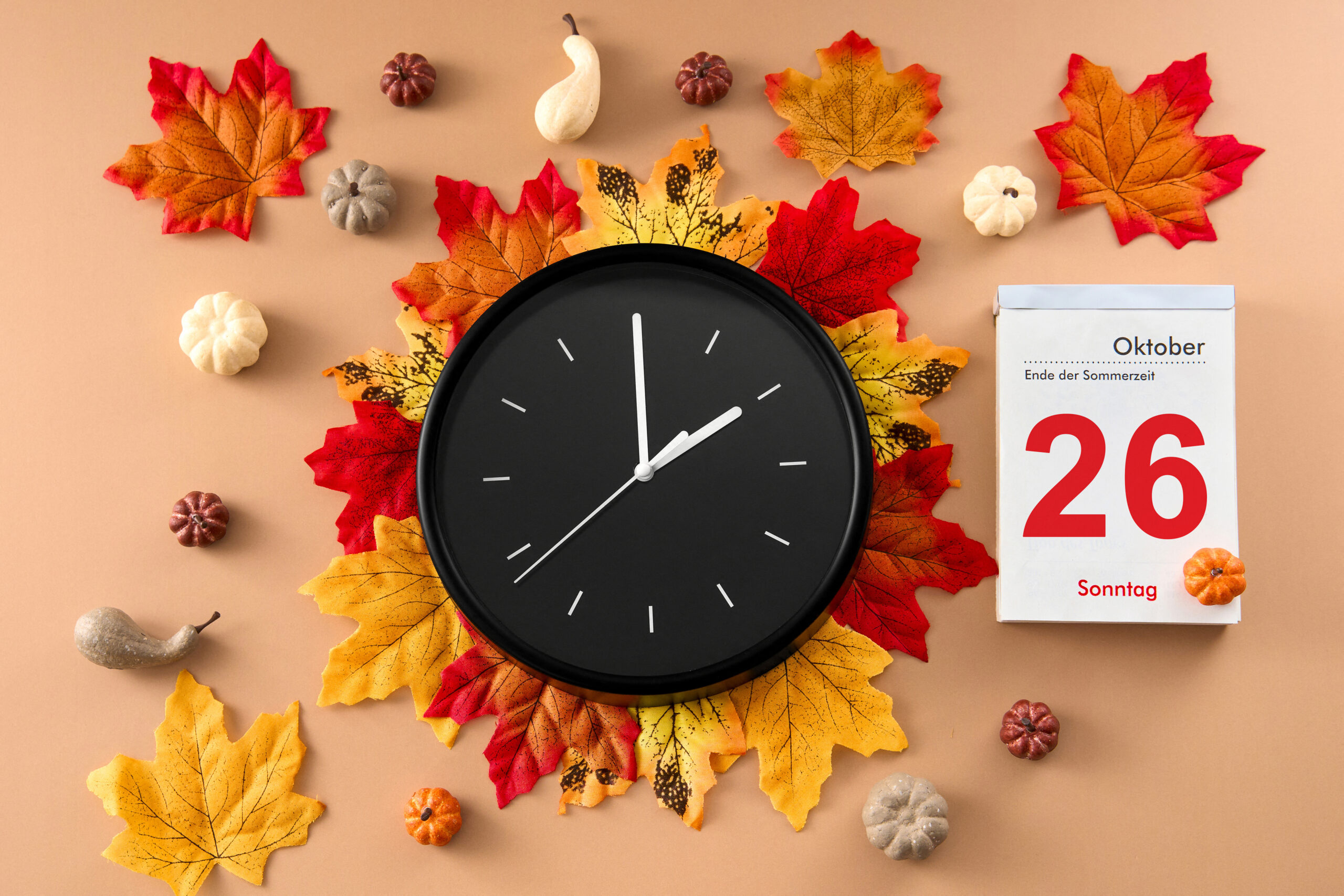 WINTERZEIT BILDER SCHWARZE UHR AUF HERBSTBLÄTTERN MIT KALENDERBLATT VOM 26. OKTOBER – BEGINN DER WINTERZEIT 2025 schwarze uhr auf herbstblättern mit kalenderblatt vom 26. oktober – beginn der winterzeit 2025
