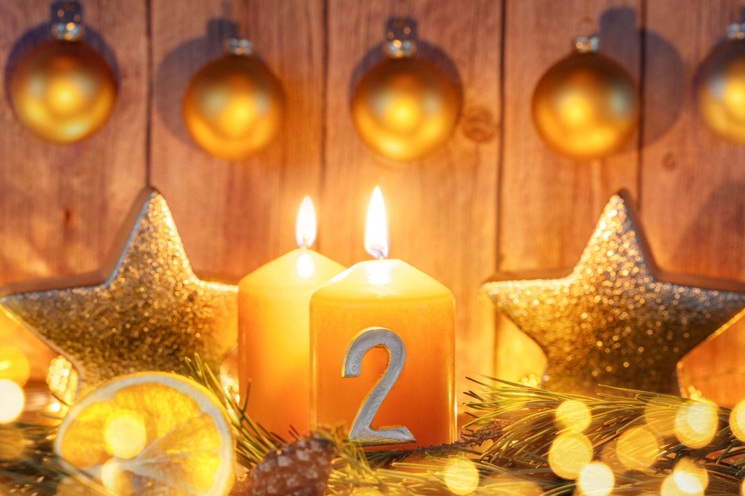 zwei leuchtende adventskerzen mit der zahl 2, umgeben von goldener deko und tannenzweigen zum zweiten advent.