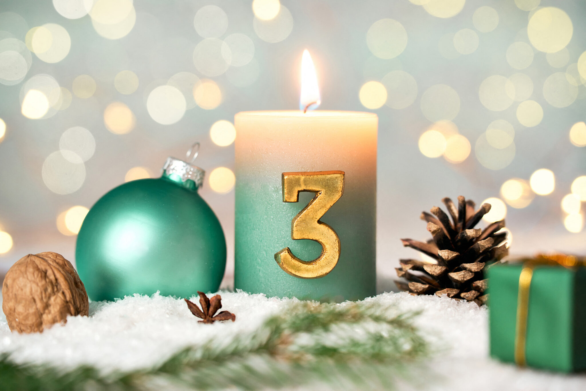 grüne kerze zum 3. advent mit weihnachtskugel, tannenzweig und deko im schnee