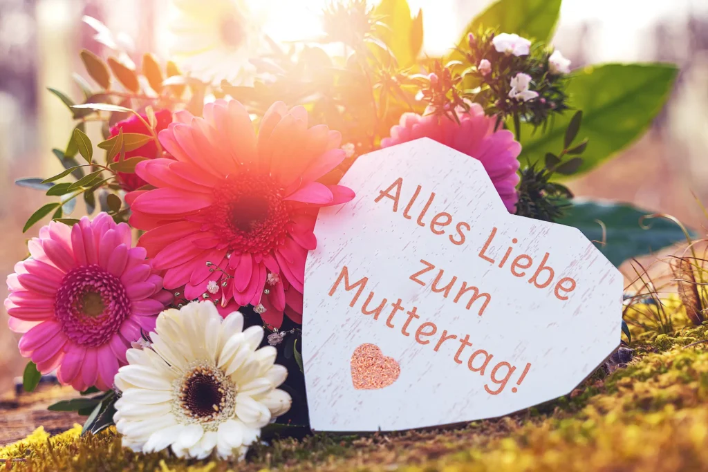 Alles Liebe zum Muttertag Muttertagsgruß auf weißer Herzkarte mit pinken und weißen Blumen im warmen Frühlingslicht.