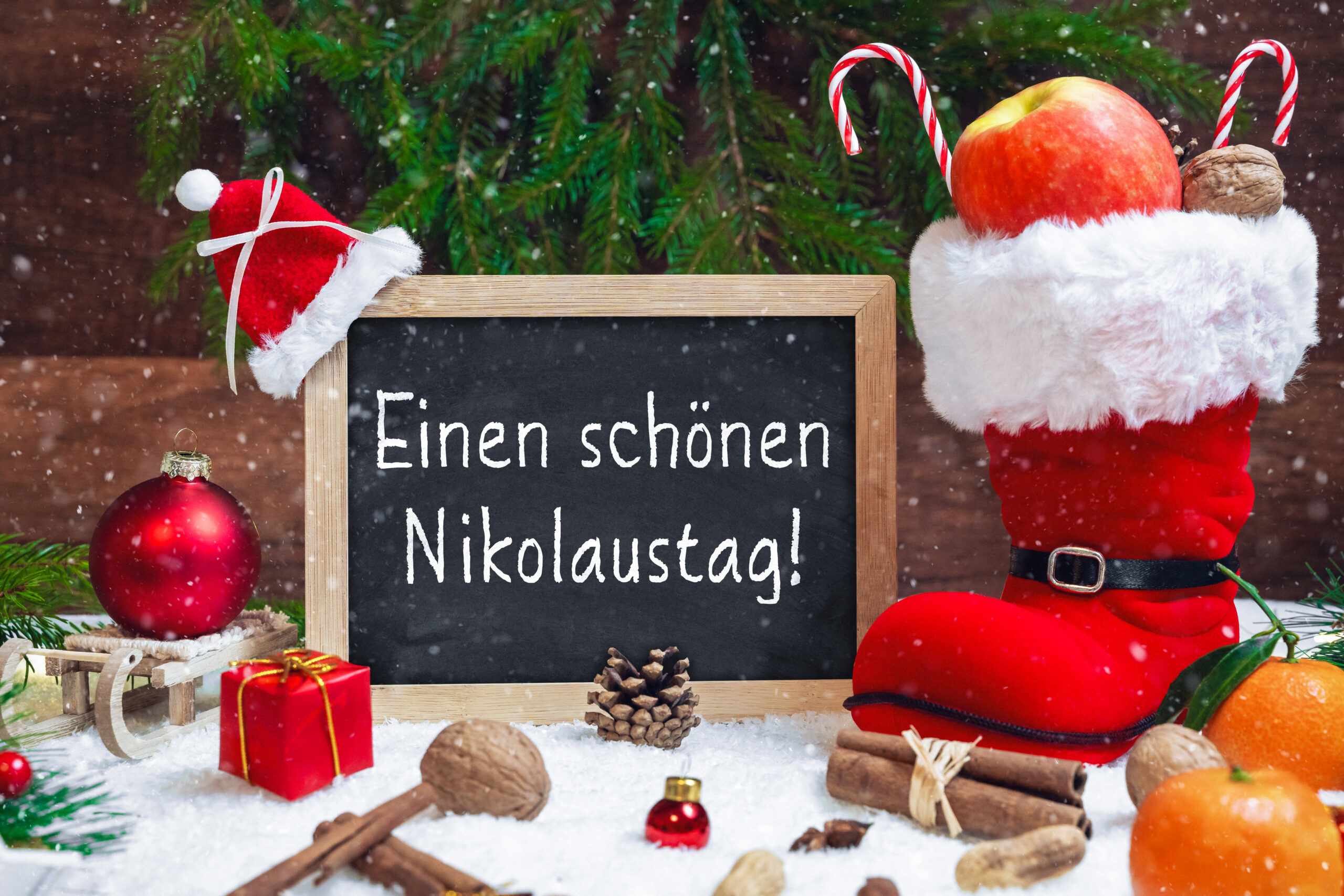 einen schönen nikolaustag mit nikolausgruß, rotem stiefel, apfel, nüssen und tafel im schnee