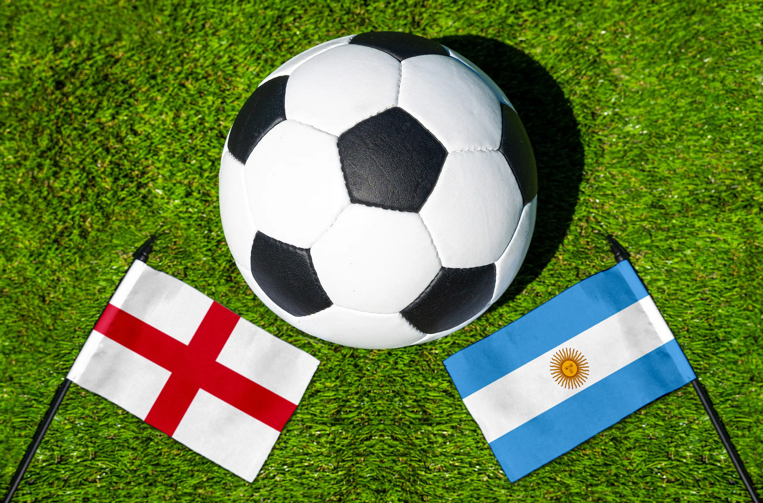 england vs argentinien mit fußball und den nationalflaggen beider länder auf grünem rasen aus der vogelperspektive.