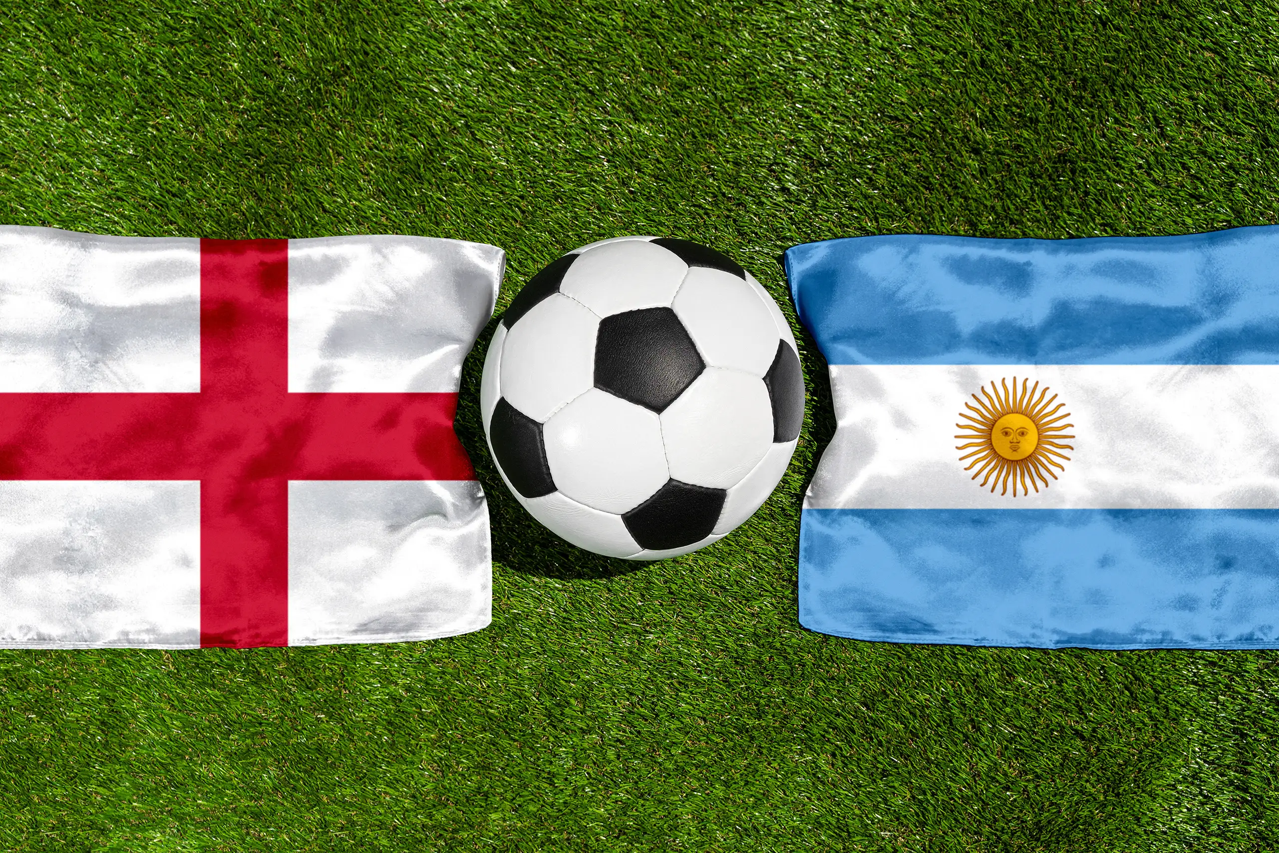 england - argentinien mit fußball zwischen den nationalflaggen auf grünem rasen in der draufsicht.