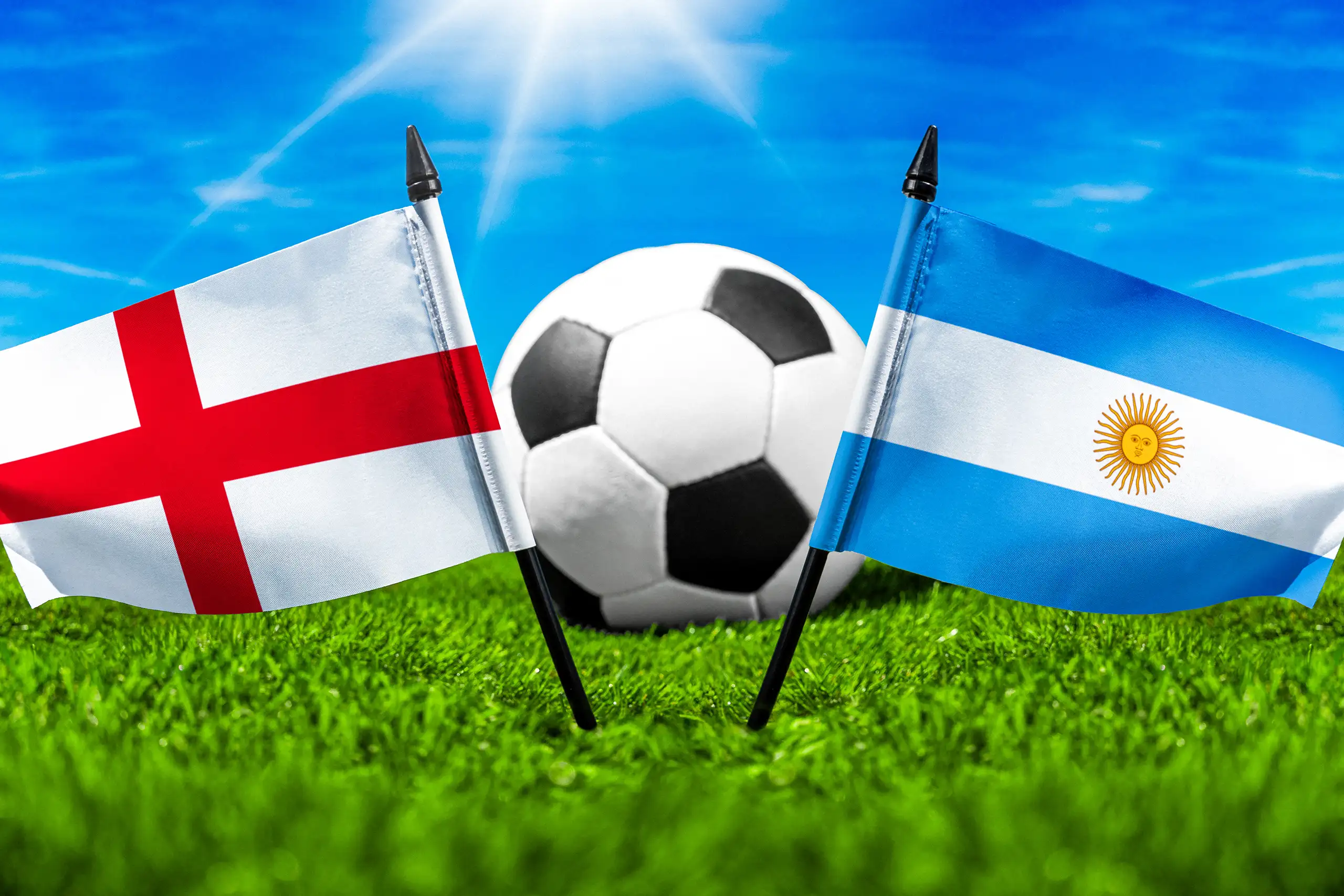england gegen argentinien mit fußball auf rasen und den nationalflaggen beider länder unter blauem himmel.