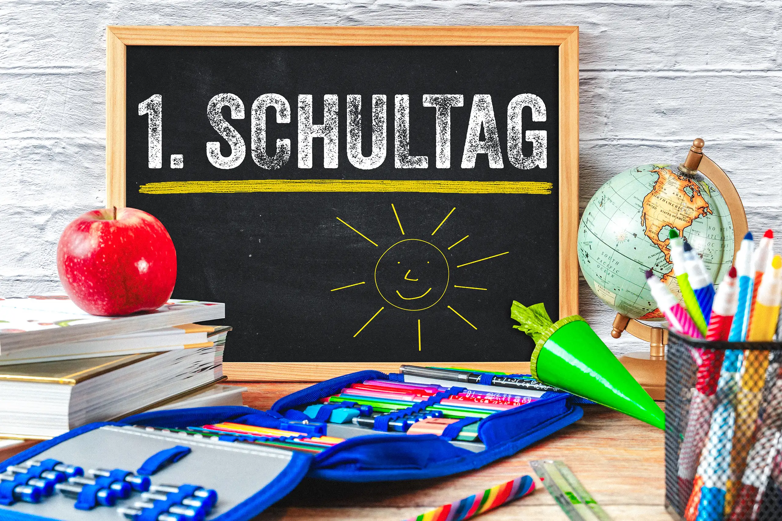 1. Schultag Bild mit schwarzer Schultafel, lächelnder Sonne, Schultüte und Schulmaterialien zur Einschulung