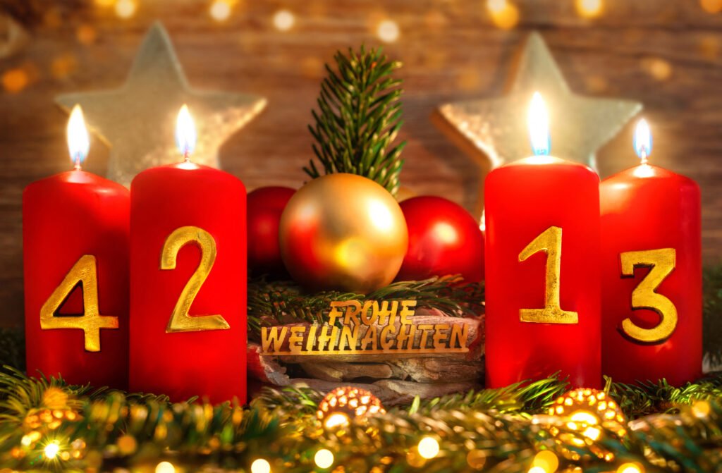 Rote Adventskerzen mit goldenen Zahlen und Schriftzug Frohe Weihnachten zwischen Tannenzweigen und Kugeln