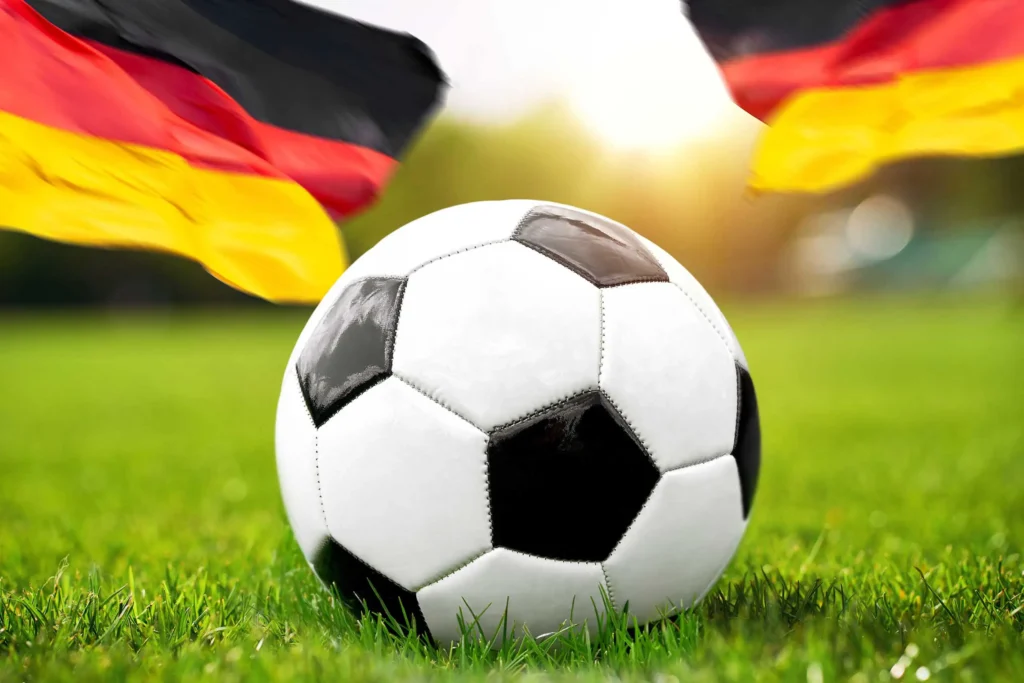 Fußball auf grünem Spielfeld mit Deutschland Fahnen im Hintergrund.