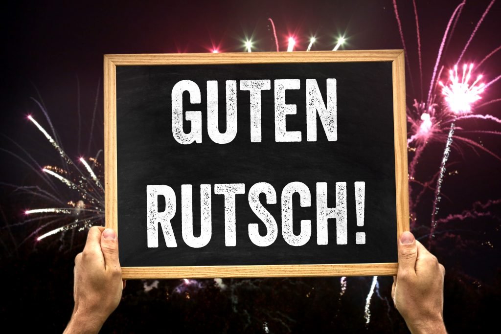 Guten Rutsch! Schild vor leuchtendem Feuerwerk
