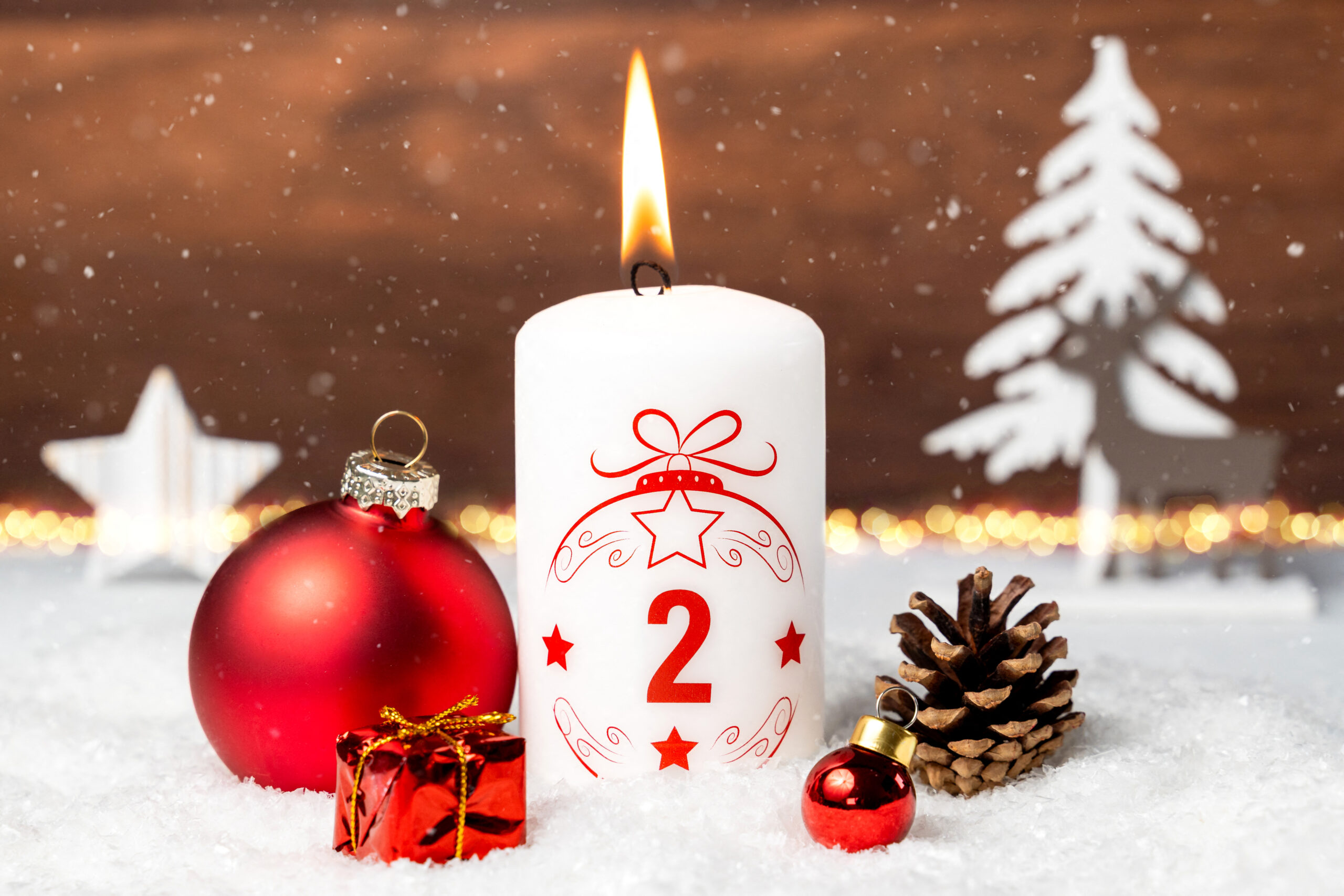 weiße kerze mit rotem motiv zum 2. advent, dekoriert mit tannenzapfen, kugeln und schnee zum 2. adventsabend