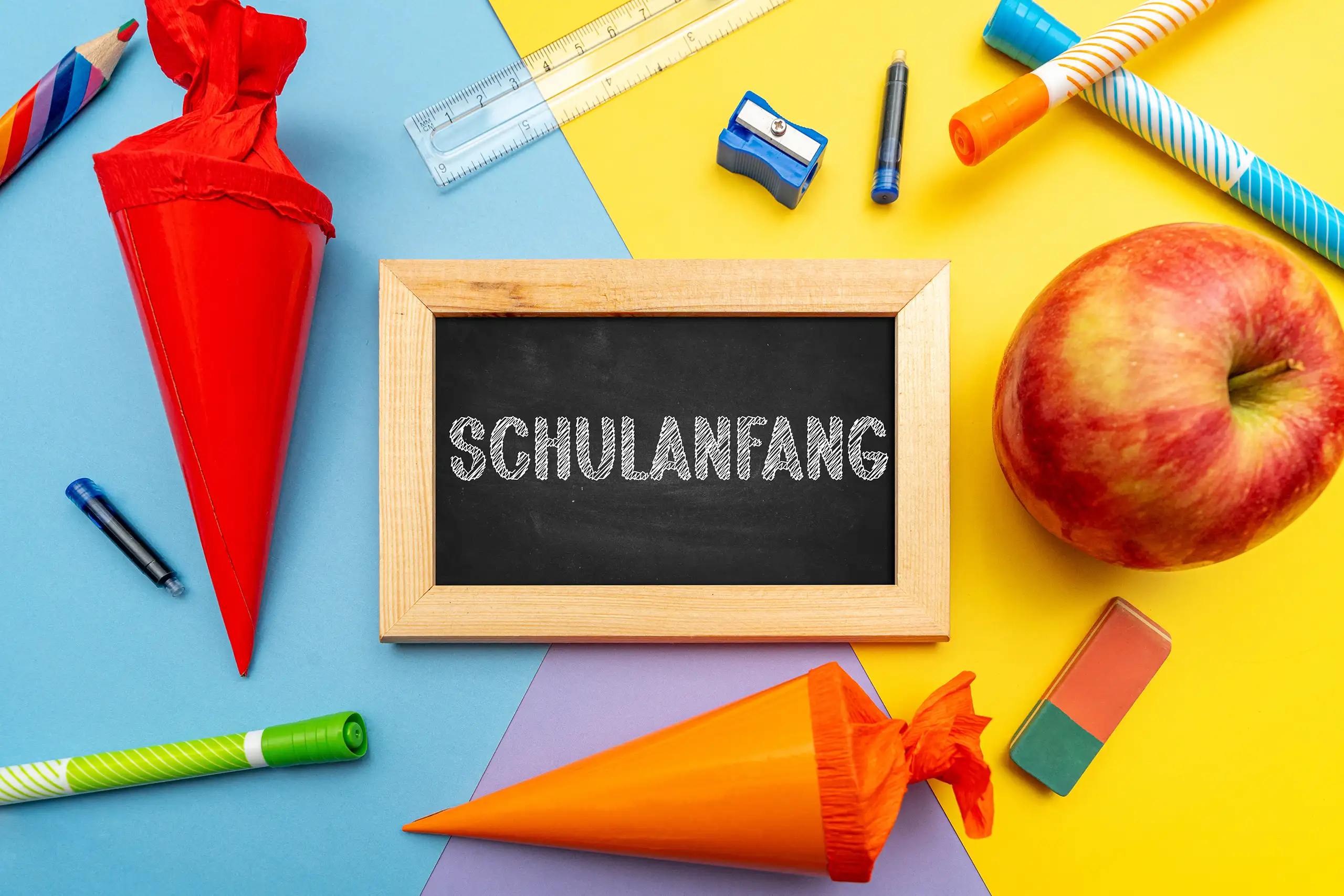 Schulanfang Bild mit Schultafel, zwei bunten Schultüten, Apfel und Schulmaterial zum Schulbeginn und ersten Schultag