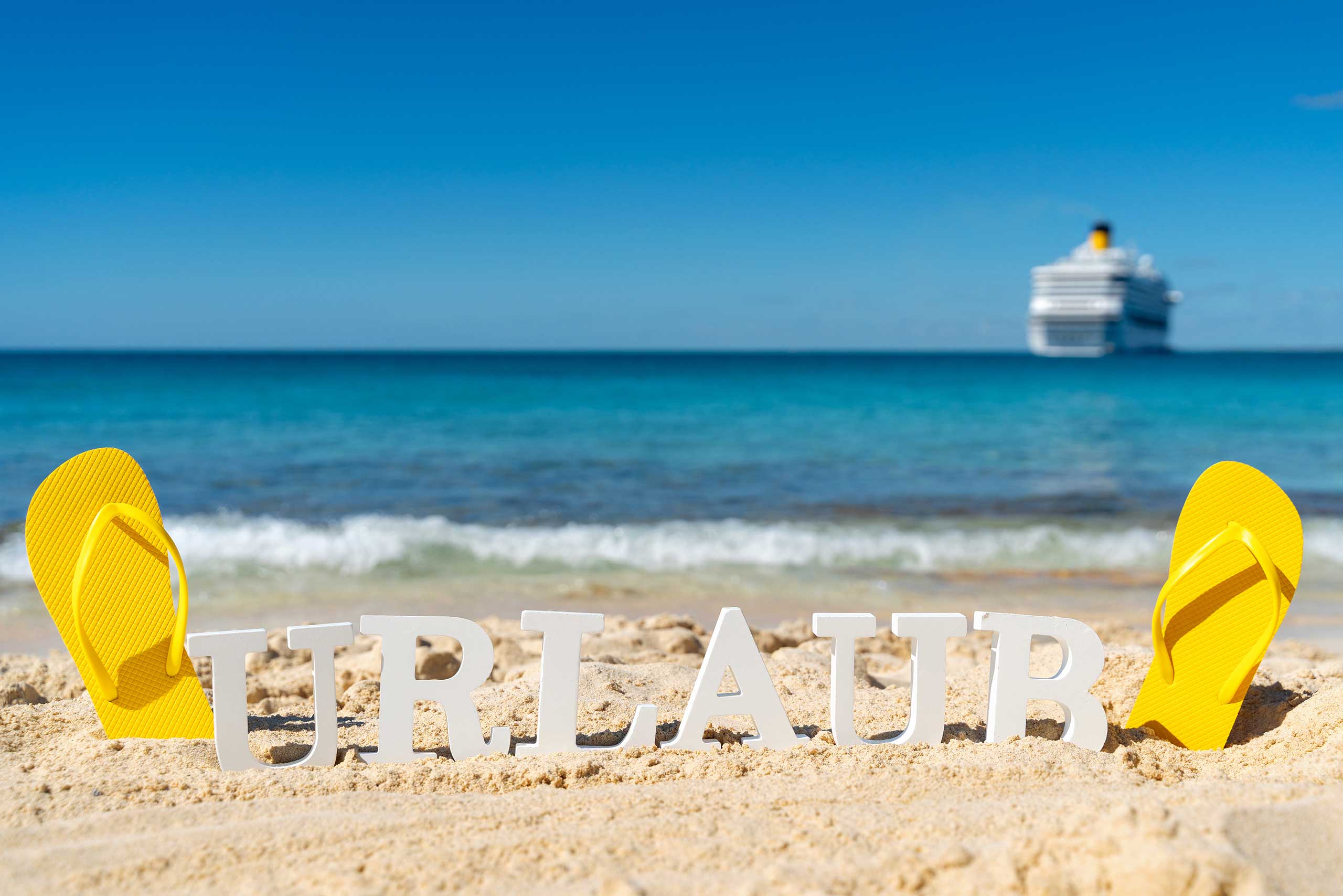 urlaub bilder schriftzug im sand am strand mit flip flops und meer im hintergrund sommer urlaub bild