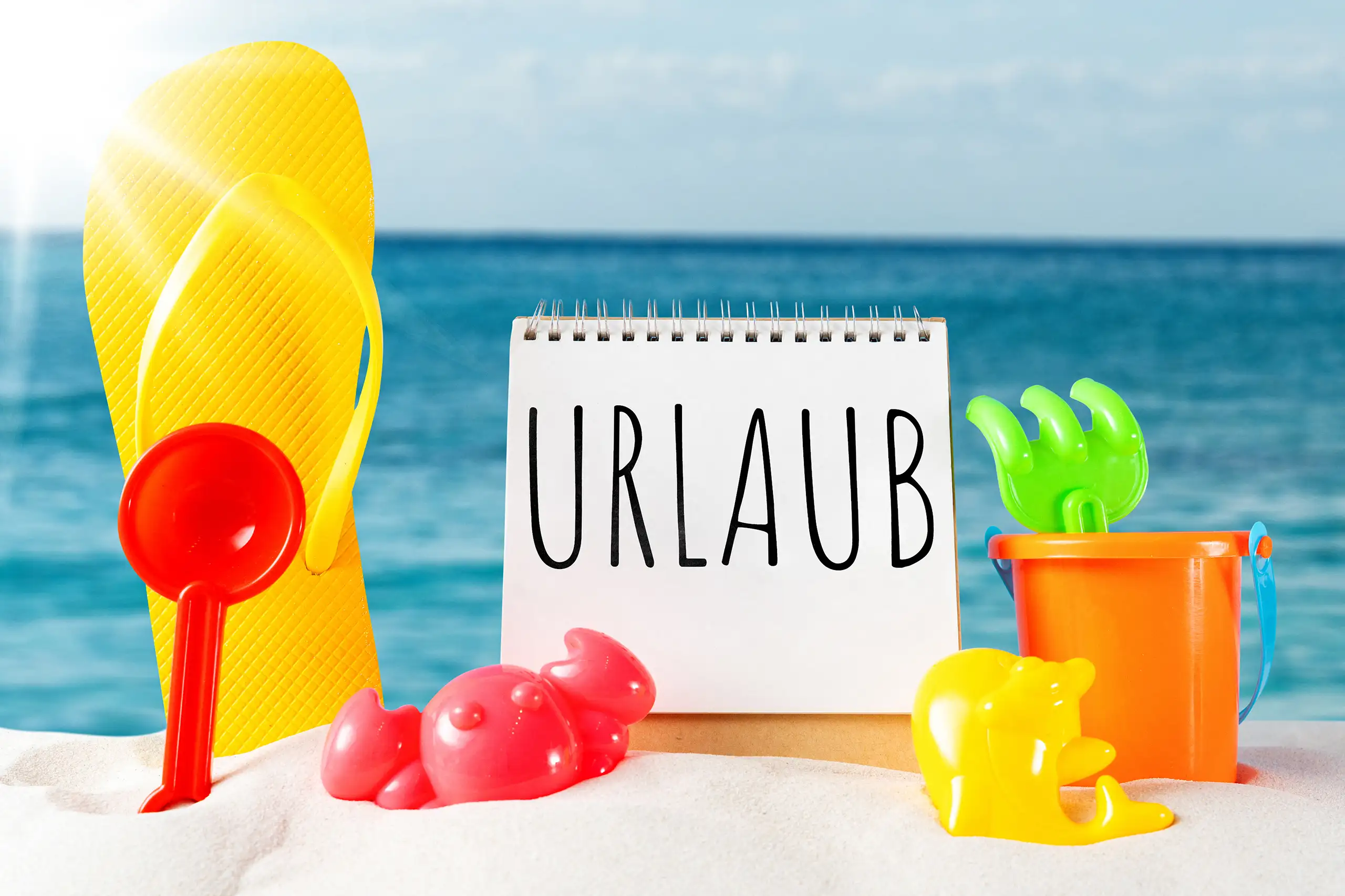 Urlaub Bild mit Schriftzug auf einem Notizblock, Strandspielzeug, Sand und blauem Meer