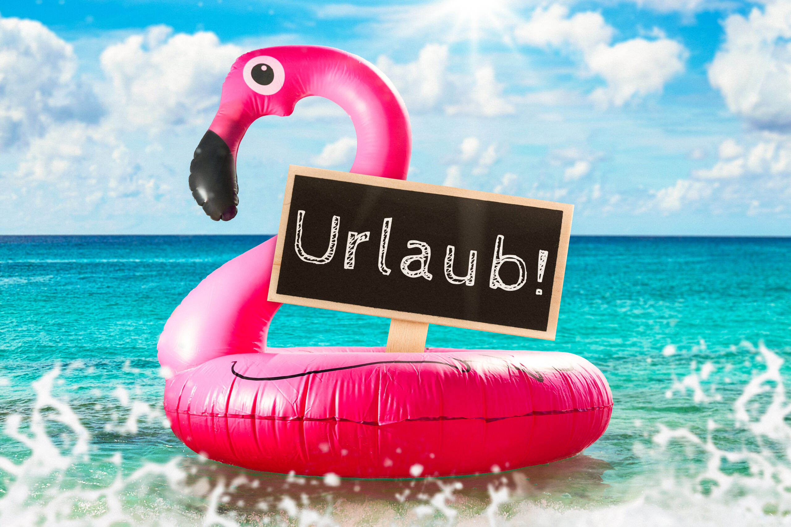 URLAUB BILDER AUFBLASBARER PINKER FLAMINGO IM MEER MIT EINEM SCHILD, AUF DEM URLAUB STEHT, WELLEN UND SONNE IM HINTERGRUND. aufblasbarer pinker flamingo im meer mit einem schild, auf dem urlaub steht, wellen und sonne im hintergrund.
