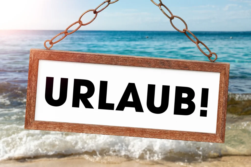 hängendes urlaubsschild mit schwarzem schriftzug vor meer, wellen und sandstrand