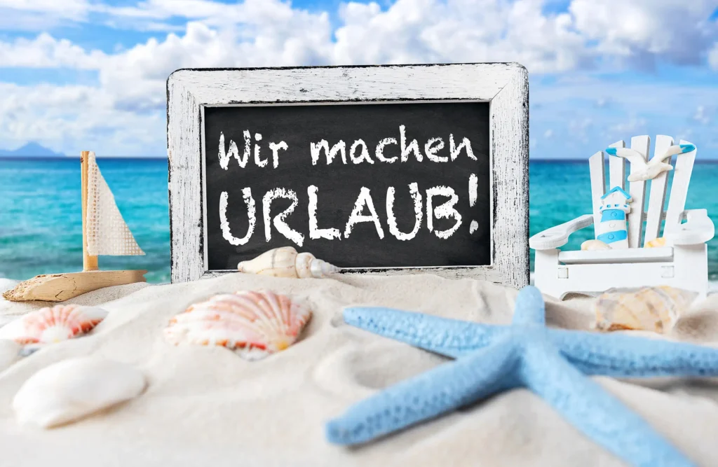 wir machen urlaub schriftzug auf schwarzer kreidetafel im sand vor dem meer