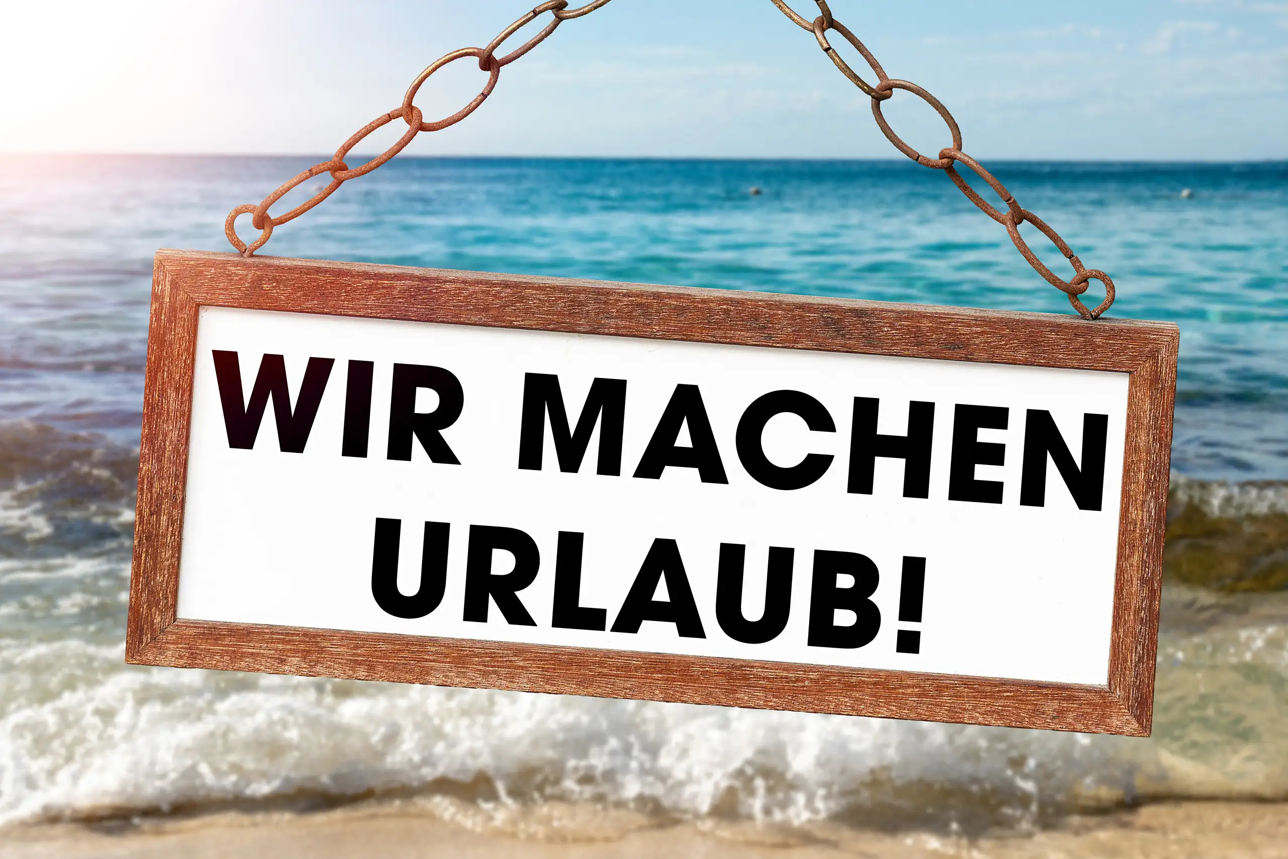Wir machen Urlaub Bild mit großem Hängeschild vor Strand, Wellen und blauem Meer