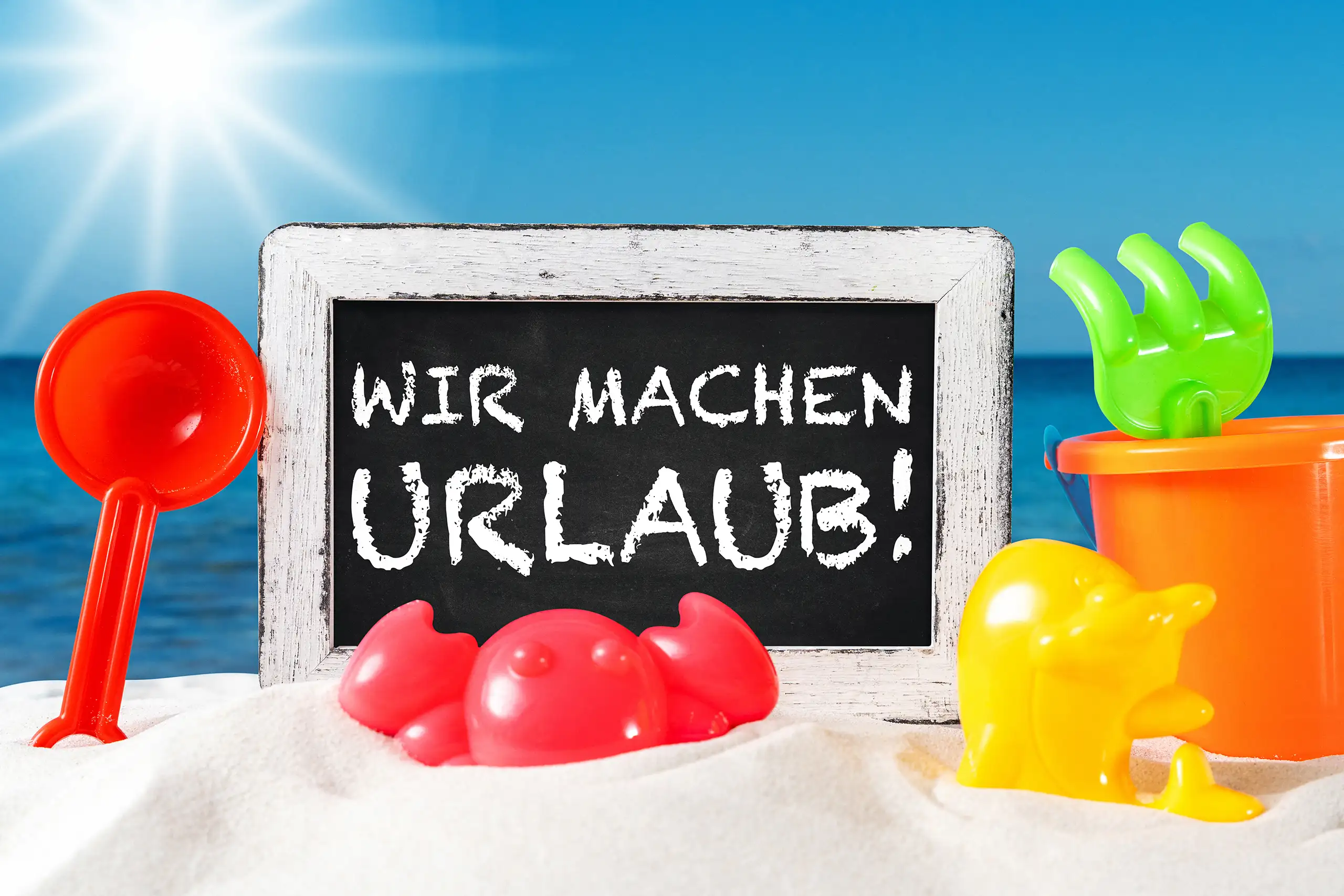 Wir machen Urlaub Bild mit schwarzer Kreidetafel, Strandspielzeug, Sand und blauem Meer