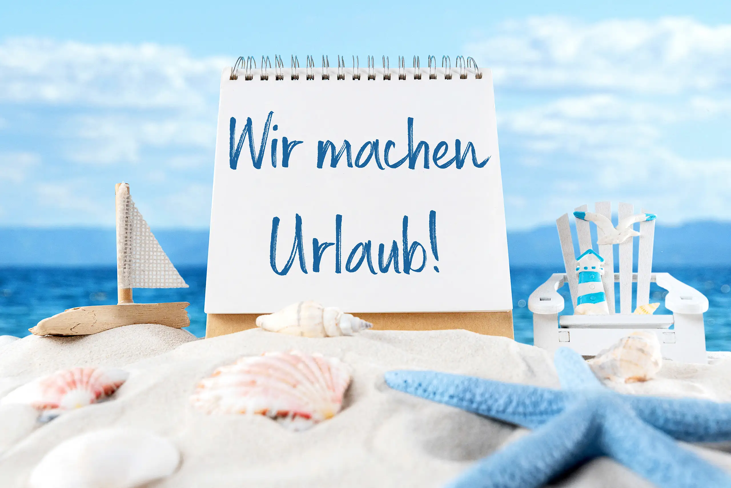 Wir machen Urlaub Schriftzug auf einem Spiralblock im Sand vor dem Meer