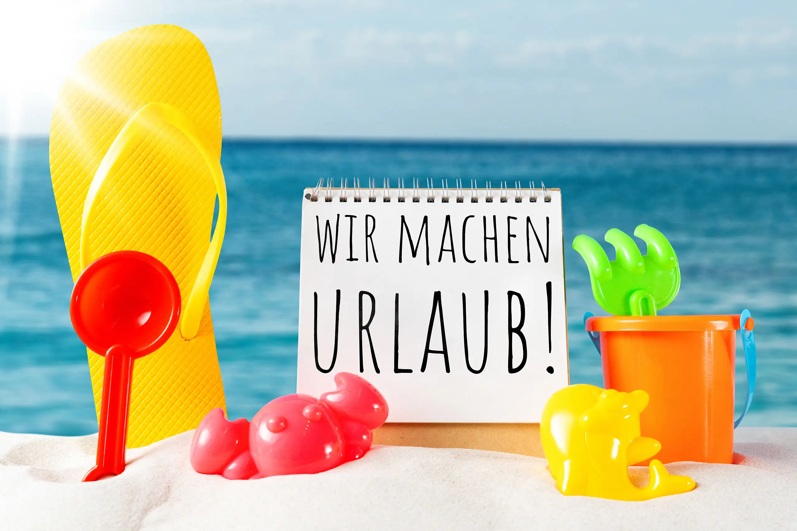 Wir machen Urlaub Bild mit Notizblock, Flip-Flops, Strandspielzeug, Sand und blauem Meer